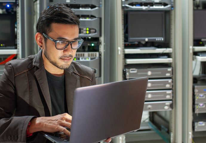 Cyber Security Specialist mit Laptop in einem Serverraum.