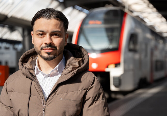 Mohammet Durmus, der an der BBS/BVS das Handelsdiplom HWD absolviert hat und heute bei der SBB arbeitet steht am Bahnhof vor einem Zug.