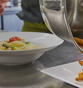 In der Küche des Restaurants Roter Platz in St. Gallen wird ein Teller mit knusprigen Pommes frites und buntem Gemüse angerichtet, während im Hintergrund weitere Gerichte für den Service vorbereitet werden.